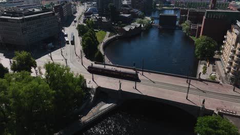 Vista-Aérea-De-Un-Tranvía-Cruzando-Un-Puente,-Revelando-El-Paisaje-Urbano-De-Tampere,-Finlandia---Inclinación,-Disparo-De-Drone