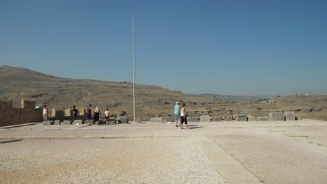 Tourists-on-top-of-Lindos-Acropolis,-Hills-in-background