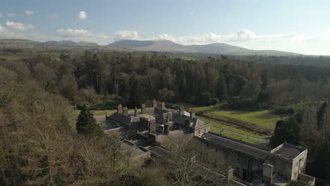 Aerial-over-the-hidden-glynllifon-estate,-surrounded-by-trees-and-overlooked-by-nearby-hills-of-snowdonia