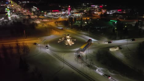 Vista-Aérea-Alrededor-De-Una-Rotonda-En-La-Iluminada-Ciudad-De-Kuusamo,-Noche-De-Invierno-En-Finlandia---Dando-Vueltas,-Disparo-De-Drones