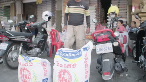 Man-carrying-big-bag-of-rice-outside-an-outdoor-rice-market-stall-in-Cambodia