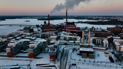 Luftaufnahme-Um-Rauchende-Schornsteine-In-Ruoholahti,-Wintersonnenuntergang-In-Helsinki,-Finnland---Kreisend,-Drohnenaufnahme