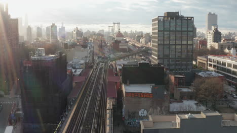 Fliegen-Sie-über-Die-Erhöhte-U-Bahn-Strecke-Mit-Der-Williamsburg-Brücke-Im-Hintergrund