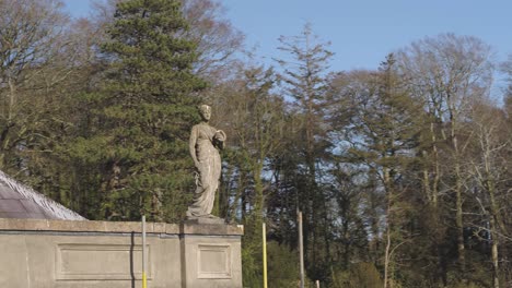 Luftnahaufnahme-Einer-Statue-Auf-Dem-Dach-Des-Glynllifon-Anwesens-Mit-Himmel-Und-Bäumen-Im-Hintergrund