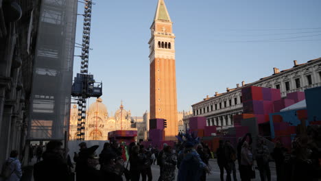 Goldene-Stunde-Auf-Dem-Markusplatz-Während-Der-Karnevalszeit,-Schräger-Blick-Auf-Den-Glockenturm-Des-Markusplatzes,-Menschen-Versammeln-Sich-In-Karnevalskostümen