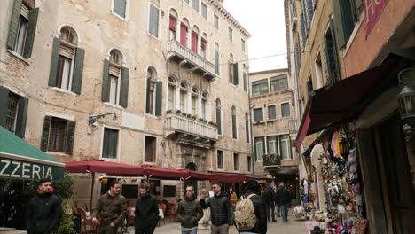 Calle-Estrecha-Y-Concurrida-Con-Pizzería-Y-Tienda-De-Regalos-En-Venecia,-Carnaval-De-Invierno,-Inclinación.