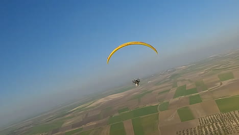 Die-Luftaufnahme-Folgt-Einem-Motorgleitschirm,-Der-Hoch-über-Landwirtschaftlichen-Nutzflächen-Fliegt