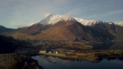 Vista-Panorámica-Aérea-Del-Hotel-Isles-Of-Glencoe-Con-El-Lago-Och-Leven-Y-Las-Hermosas-Tierras-Altas-Escocesas-Y-El-Pico-Nevado-Al-Atardecer,-Escocia