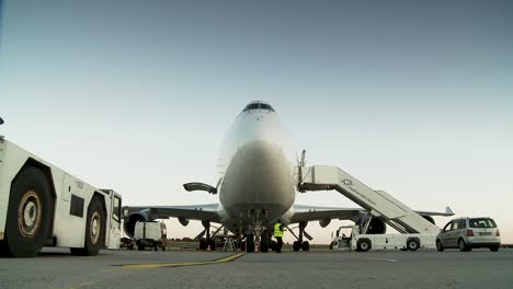 Vista-A-Nivel-Del-Suelo-De-Un-Avión-Comercial-En-Un-Aeropuerto-Durante-Las-Primeras-Horas-De-La-Tarde-Con-Trabajadores-Y-Vehículos-Alrededor