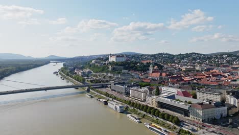 Vuele-Sobre-El-Río-Danubio-Con-Vistas-Aéreas-Del-Paisaje-Urbano-Del-Castillo,-El-Puente-Snp-Y-St.