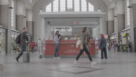 Busy-train-station-scene-with-travelers-and-a-DB-Information-desk,-conveying-a-sense-of-daily-commute-and-public-transport