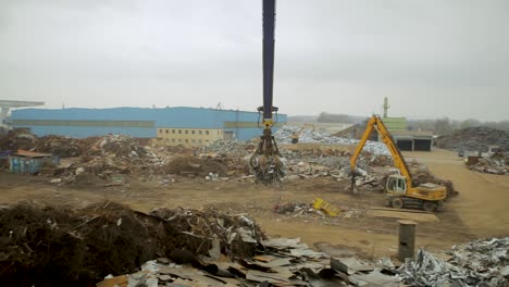 Depósito-De-Chatarra-Industrial-Con-Maquinaria-Pesada-Clasificando-Montones-De-Desechos-Metálicos-Durante-Un-Día-Nublado,-Creando-Un-Ambiente-De-Decadencia-Urbana