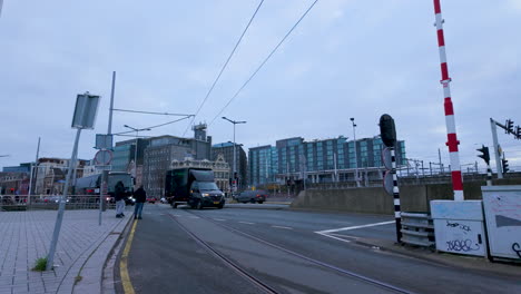 Una-Vista-De-Una-Calle-De-La-Ciudad-Con-Líneas-De-Tranvía,-Una-Barrera-De-Cruce-De-Ferrocarril-Y-Varios-Edificios-Urbanos,-Posiblemente-Cerca-De-Un-Centro-De-Transporte-Principal-O-De-Una-Estación-Central-En-Ámsterdam