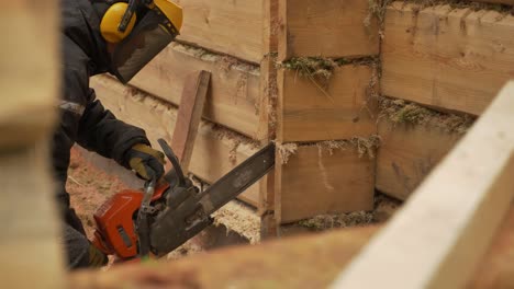 Trabajador-Con-Equipo-De-Seguridad-Está-Cortando-Con-Motosierra-Una-Casa-De-Troncos-De-Madera