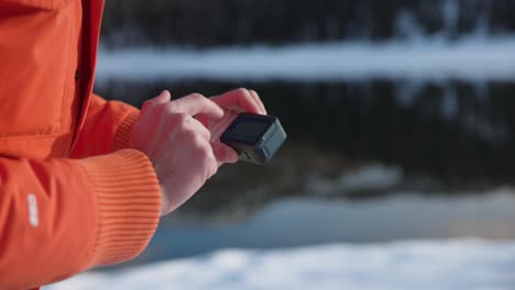 Una-Persona-Con-Chaqueta-Naranja-Toca-La-Pantalla-Táctil-De-La-Cámara-De-Acción-Insta360-Ace-Pro-Al-Aire-Libre-En-Invierno