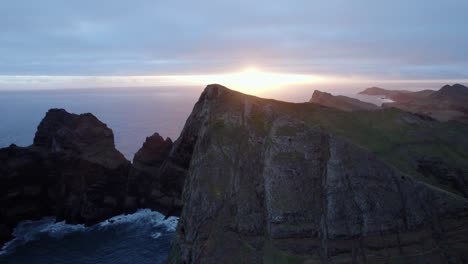 Drone-flying-over-the-blue-ocean-during-sunset-at-the-coastal-rugged-shore-at-Madeira