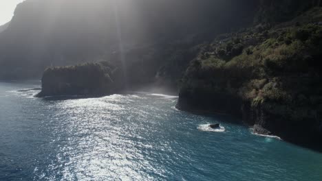 Drone-Aéreo-Disparado-Sobre-El-Mar-Sobre-Un-Rayo-De-Luz-Brilla-Sobre-El-Tranquilo-Océano-Azul-Junto-A-Acantilados-Verdes-En-Madeira