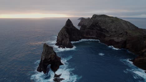 Drone-flying-over-the-wavy-sea-while-rugged-coastal-cliffs-are-visible-in-the-background