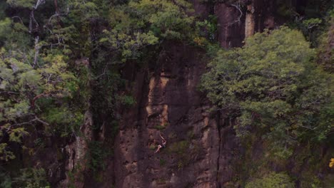 Un-Escalador-Con-Cuerdas-Levanta-El-Pulgar-Hacia-El-Dron-Antes-De-Descender-En-Rapel-Mientras-El-Dron-Retrocede-Revelando-Una-Amplia-Vista-Del-Paisaje.