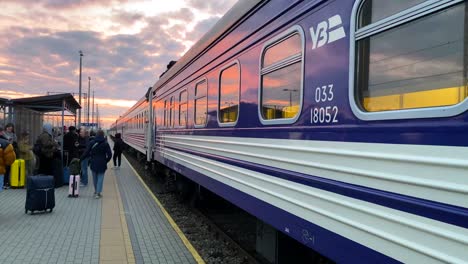 Zug-Der-Ukrainischen-Eisenbahn-Ukrzaliznycia-Mit-Wunderschönem-Rosafarbenen-Sonnenaufgangshimmel-Am-Bahnhof-Chelm-In-Polen,-Ukrainische-Flüchtlinge-Warten-Am-Frühen-Morgen-Darauf,-In-Den-Zug-Nach-Kiew-In-Der-Ukraine-Einzusteigen,-4k-Kippt-Nach-Oben