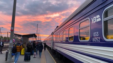 Zug-Der-Ukrainischen-Eisenbahn-Ukrzaliznycia-Mit-Wunderschönem-Rosafarbenen-Sonnenaufgangshimmel-Am-Bahnhof-Chelm-In-Polen,-Ukrainische-Flüchtlinge-Warten-Darauf,-Am-Frühen-Morgen-In-Den-Zug-Nach-Kiew-Einzusteigen,-4K-Aufnahme