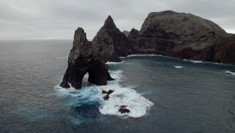 Drone-flying-over-the-wavy-sea-while-rugged-coastal-cliffs-are-visible-in-the-background