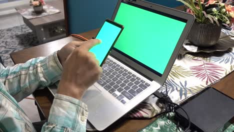 A-man-swiping-the-screen-of-a-mobile-phone-in-front-of-a-computer