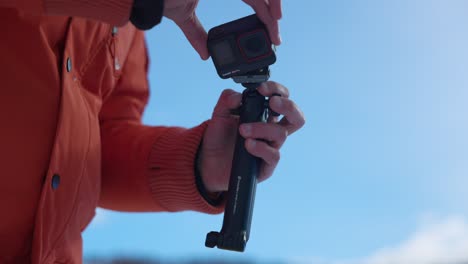 Person-In-Orangefarbener-Jacke-Hält-Die-Insta360-Actionkamera-Und-Nimmt-Sie-Mit-Einem-Magnetclip-Vom-Griff-Ab