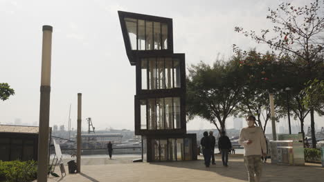 People-walk-past-unique-stacked-container-building-art-installation-in-park-on-sunny-day