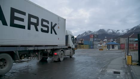 White-semi-truck-at-industrial-Ushuaia-port-during-dusk,-mountains-in-background,-overcast-sky