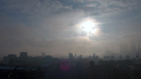 Die-Frostigen-Dächer-Eines-East-End-Anwesens-Sind-In-Eiskalten-Nebel-Gehüllt,-Während-Die-Sonne-Durch-Die-Wolken-über-Einem-Verdeckten-Finanzviertel-Von-Canary-Wharf-Bricht