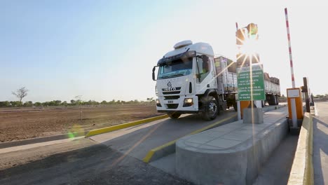 Sunlight-flares-around-a-cargo-truck-at-a-toll-booth,-clear-blue-sky,-lens-flare-effect