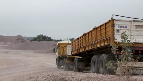 Camión-Volquete-Amarillo-Conduciendo-A-Través-De-Una-Zona-Minera-Con-Montículos-De-Tierra,-Cielo-Nublado,-Toma-Estática