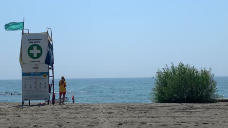 Vista-Trasera-De-Un-Salvavidas-Parado-En-La-Playa-Para-Proteger-A-Los-Turistas-En-Cualquier-Accidente-Inusual-Con-Un-Hermoso-Paisaje-Marino-Durante-Un-Día-Soleado