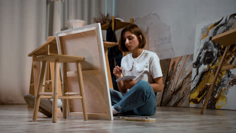 Young-woman-sitting-on-the-floor-with-canvas