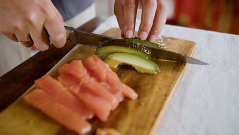 Close-up-view-of-asian-couple-hands-making-sushi-and-cutting-avocado-on-top-of-a-kitchen-board-at-home