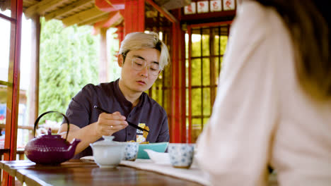 Asiatischer-Mann-Isst-Ramen,-Während-Er-Mit-Seinem-Partner-Spricht-Und-An-Einem-Tisch-In-Einem-Japanischen-Haus-Sitzt