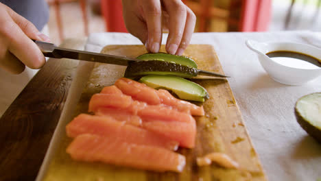 Close-up-view-of-asian-couple-hands-making-sushi-and-cutting-avocado-on-top-of-a-kitchen-board-at-home