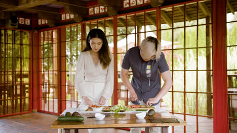 Pareja-Asiática-Preparando-Sushi-Y-Cortando-Pescado-Fresco-Sobre-Una-Tabla-De-Cocina-En-Casa