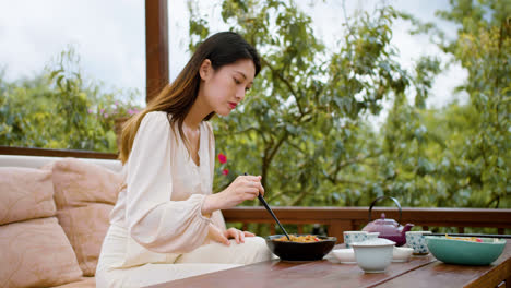 Asiatische-Frau-Isst-Ramen,-Während-Sie-Mit-Ihrem-Partner-Spricht,-Der-Auf-Einer-Japanischen-Gartenveranda-Sitzt