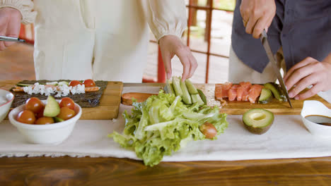 Front-view-of-asian-couple-hands-making-sushi-and-cutting-avocado-on-top-of-a-kitchen-board-at-home