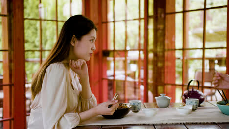 Asian-couple-eating-ramen-and-talking-while-they-are-sitting-at-a-table-with-cups-of-tea-in-a-japanese-home