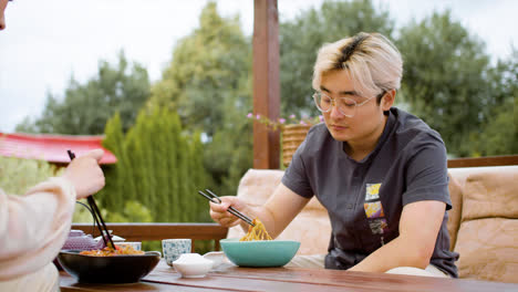 Asian-man-eating-ramen-while-she-is-talking-with-her-partner-sitting-on-a-japanese-garden-porch