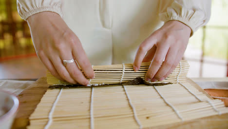 Vista-De-Cerca-De-Las-Manos-De-Una-Mujer-Asiática-Haciendo-Sushi-Sobre-Una-Tabla-De-Cocina-En-Casa