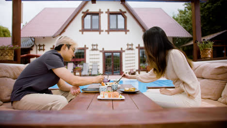 Side-view-of-asian-couple-eating-sushi-while-they-are-talking-sitting-on-a-japanese-garden-porch