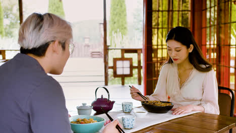 Asiatisches-Paar-Isst-Ramen-Und-Unterhält-Sich,-Während-Sie-Mit-Tassen-Tee-An-Einem-Tisch-In-Einem-Japanischen-Haus-Sitzen