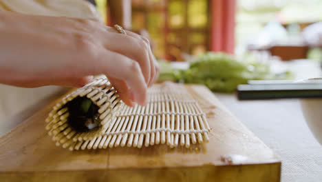 Vista-De-Cerca-De-Las-Manos-De-Una-Mujer-Asiática-Haciendo-Sushi-Sobre-Una-Tabla-De-Cocina-En-Casa