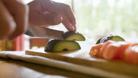 Vista-De-Cerca-De-Las-Manos-De-Un-Hombre-Asiático-Cortando-Aguacate-Sobre-Una-Tabla-De-Cocina-En-Casa