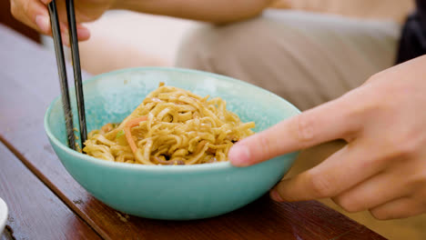 Close-up-view-of-hands-of-a-man-picking-up-noodles-with-chopsticks-from-the-plate-on-a-table-outdoors