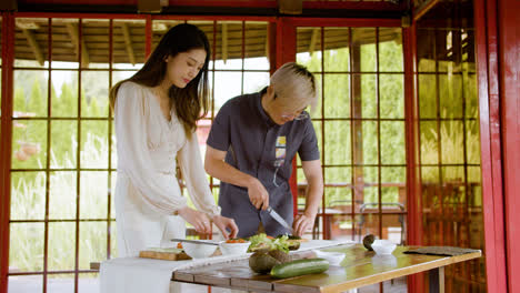 Asian-couple-making-sushi-and-cutting-fresh-cucumber-and-fish-on-top-of-a-kitchen-board-at-home